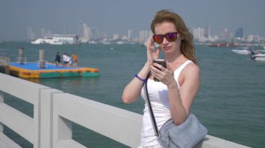 kadın güneş gözlüğü, iskelede duran onun smartphone kullanır. arka plan bulanıklık,