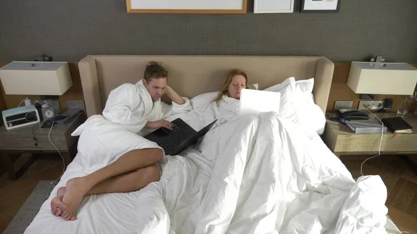 Casal jovem deitado na cama usando computador portátil, conversando on-line, menina e homem no quarto. Bom dia. — Fotografia de Stock