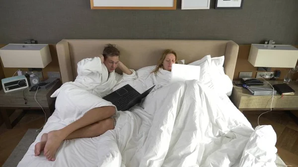 Pasangan muda berbaring di tempat tidur menggunakan komputer laptop, chatting online, gadis dan pria di kamar tidur. Pagi — Stok Foto
