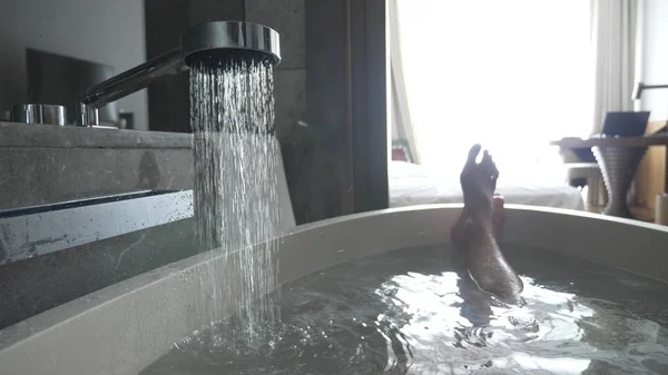 Piernas mans en un baño de hotel. agua caliente vierte en el baño y de ella sale vapor . — Foto de Stock