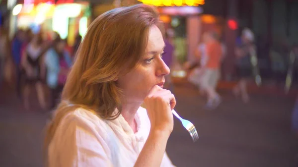 Mujer joven y hermosa comiendo postre, sentada afuera en una cafetería o terraza. Una mujer admira un corte de fruta . — Foto de Stock