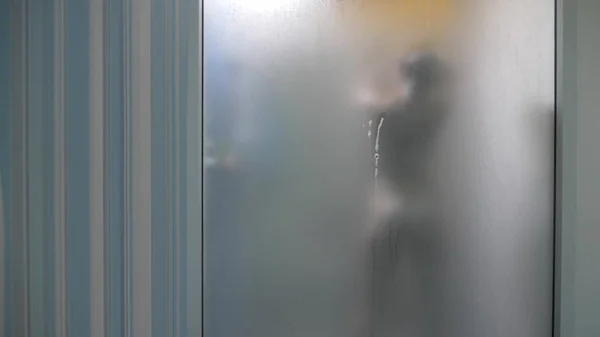 Женщина за размытым стеклом. Девочка готовится принять душ. Женщина в ванной. мужчина наблюдает, как женщина принимает душ через стеклянную стену в душе . — стоковое фото