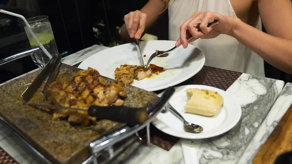 Seseorang untuk berbicara dan makan malam di bar menghadap pencakar langit, di malam hari, tangan Perempuan memotong sepotong steak dengan pisau dan garpu . — Stok Foto