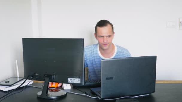 Un hombre sentado en un escritorio en casa, trabajando en el ordenador de casa y portátil . — Vídeo de stock