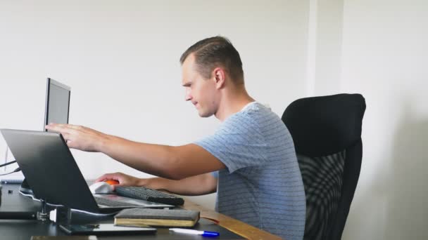 Een man zit achter een bureau thuis, thuis werken, computer en laptop. — Stockvideo