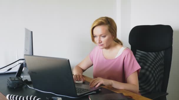Όμορφη νεαρή γυναίκα που εργάζεται σε ένα φορητό υπολογιστή και υπολογιστή ενώ κάθεται σε ένα γραφείο. — Αρχείο Βίντεο