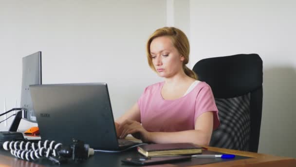 Vacker ung kvinna som arbetar på en bärbar dator och dator medan du sitter vid ett skrivbord. — Stockvideo