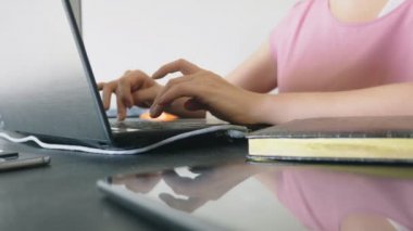 bir masada otururken bir dizüstü bilgisayarda çalışan kadın.