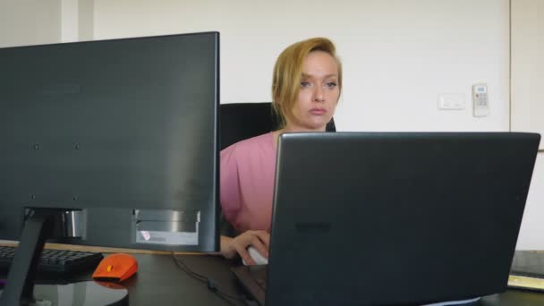 Bir masada otururken bir dizüstü bilgisayar ve bilgisayar üzerinde çalışan güzel genç kadın. — Stok video
