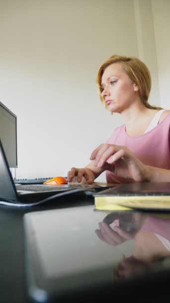 Gyönyörű fiatal nő dolgozik a laptop és a számítógép egy íróasztalnál ülve. — Stock videók