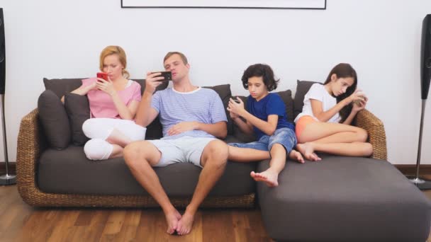 Família encantadora, mãe, pai, filha e filho estão assistindo TV na sala de estar juntos, todo mundo está olhando em seu telefone — Vídeo de Stock