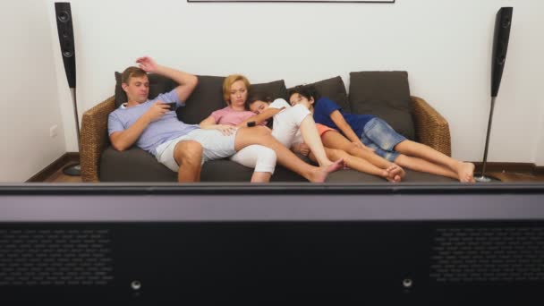Чарівна сім'я, мама, тато, дочка і син дивляться телевізор у вітальні разом, засинаючи перед телевізором — стокове відео