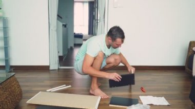 Genç bir adam bağımsız olarak mobilya evinin oturma odasında toplar. Bir adam bilgisayar masası toplar.