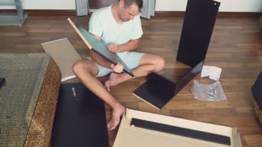 Genç bir adam bağımsız olarak mobilya evinin oturma odasında toplar. Bir adam bilgisayar masası toplar.