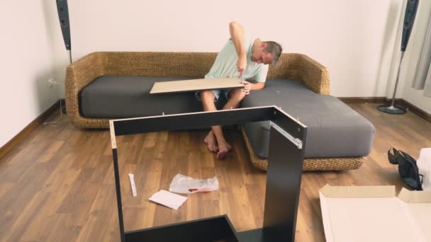 Un jeune homme recueille indépendamment des meubles dans le salon de sa maison. Un homme recueille un bureau d'ordinateur . — Video