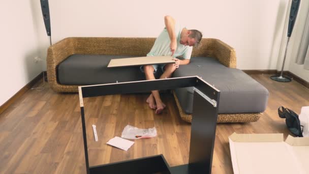 A young man independently collects furniture in the living room of his house. A man collects a computer desk. — Stock Video