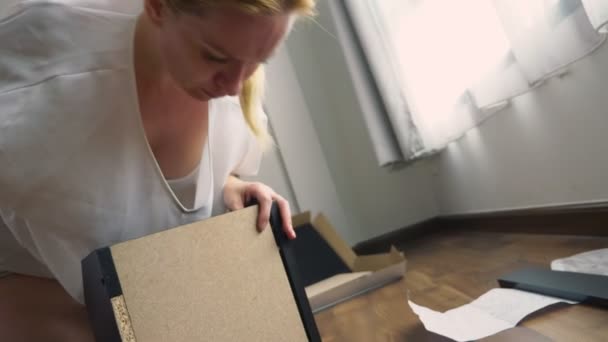 Assemblage de meubles à la maison, une femme au foyer assemble un bureau d'ordinateur à l'aide d'outils à main . — Video