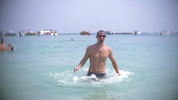 Um jovem mergulha no mar usando óculos escuros. emerge e sorri — Fotografia de Stock