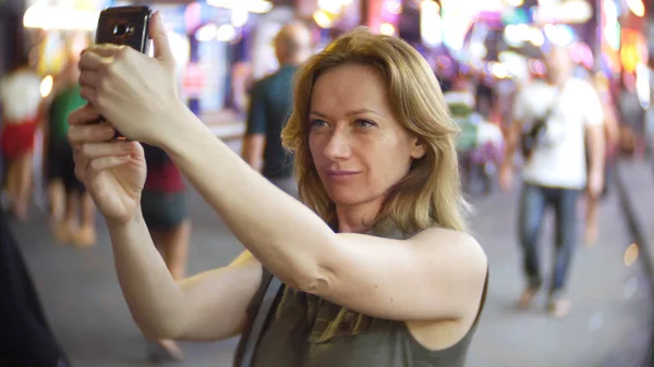 Potret wanita muda yang elegan dengan selfie di jalan yang ramai pada malam hari, latar belakang yang kabur — Stok Foto
