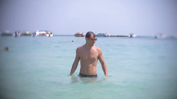Mladý muž se ponoří do moře nosí sluneční brýle. vzniká a usmívá se — Stock fotografie