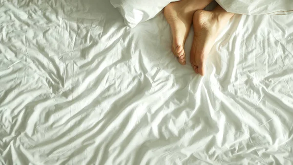 Piernas femeninas en la cama vista desde arriba, ropa de cama blanca —  Fotos de Stock