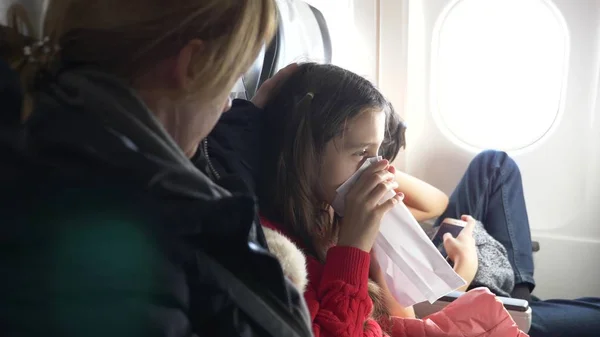 Женщина в самолете с детьми на фоне иллюминатора. самолет вошел в зону турбулентности. Девушка запаниковала, она дышит в бумажный пакет . — стоковое фото