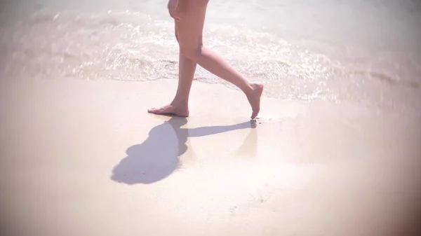 Frauenbeine plätschern ins Wasser. Mädchen läuft barfuß am Sandstrand. — Stockfoto