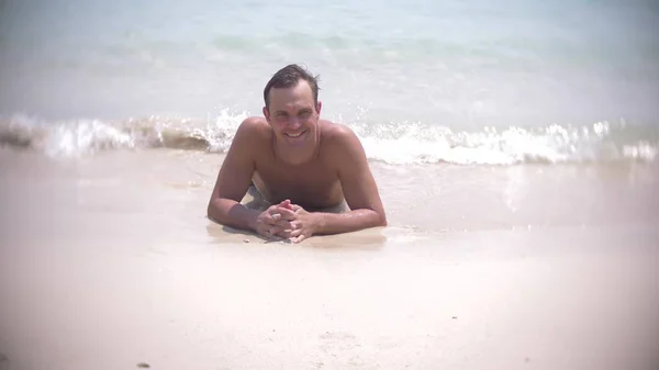 Jovem deita-se na areia branca olhando para a câmera e sorrindo — Fotografia de Stock