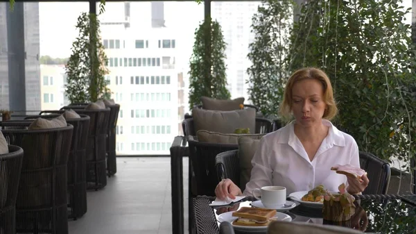 Hermosa chica elegante, desayunando en una cafetería en la terraza con una hermosa vista de los rascacielos. Una mujer tomando café caliente en la lujosa terraza de los hoteles . — Foto de Stock