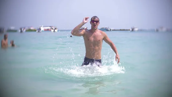 Un joven se sumerge en el mar con gafas de sol. emerge y sonríe — Foto de Stock