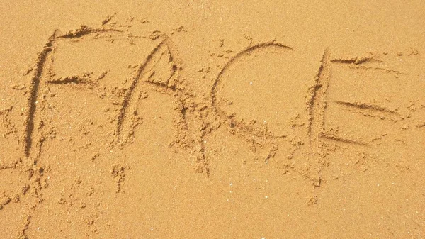 海の波は、砂に書いた銘刻文字を消去します。平面図です。単語の顔 — ストック写真