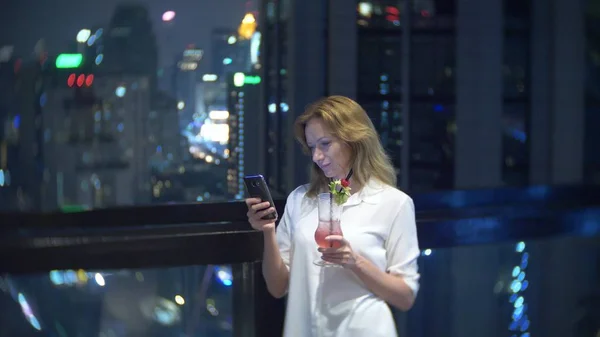 Mladá žena blond uvolňující a pití koktejlů v baru s výhledem mrakodrapy v noci. rozostření pozadí — Stock fotografie