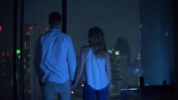 Egy fiatal pár áll a háttérben, a panoráma ablak kilátás nyílik a városra. Este éjszakai. életlenítés háttér — Stock Fotó