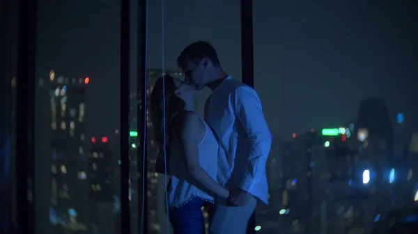 Egy fiatal pár is megcsókolta, a háttérben egy panoráma ablak kilátás nyílik a városra. Este éjszakai. életlenítés háttér — Stock Fotó
