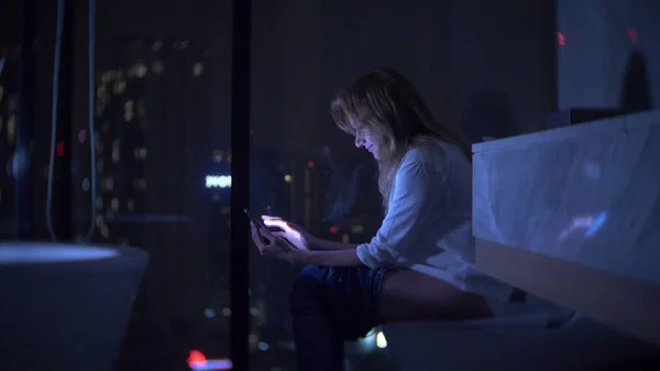 Seorang wanita duduk di toilet di toilet mewah dengan jendela panorama di malam hari dengan telepon dan bekerja . — Stok Foto