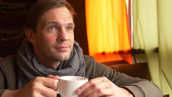 Молодой человек в шарфе, пьющий чай и улыбающийся в кафе . — стоковое фото