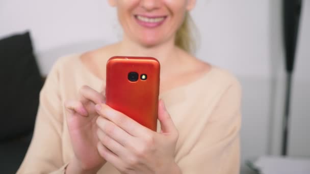 Bella ragazza utilizzare uno smartphone cellulare mentre seduto in soggiorno la sera. Felice sorridente giovane donna che chiacchiera su internet a casa . — Video Stock