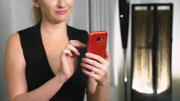 아름 다운 여자는 저녁에 거실에 앉아있는 동안 셀룰러 스마트폰을 사용 합니다. 행복 한 미소 젊은 여자 집에서 인터넷에서 채팅. — 비디오