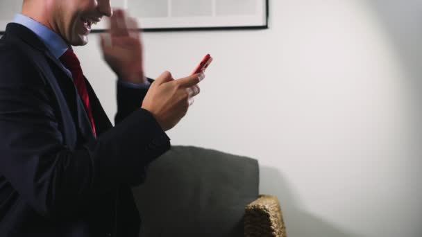 Piękny gej używać komórkowy smartphone siedząc w salonie w godzinach wieczornych. Szczęśliwy uśmiechający się młody człowiek, rozmawiania przez internet w domu. — Wideo stockowe