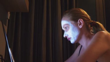 Genç kadın kozmetik maskesi yüzünde akşamları evde laptop ile çalışma. doğallığı