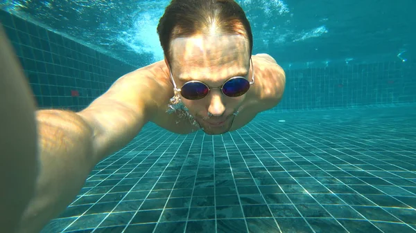 Um jovem homem bonito branco fazendo uma selfie subaquática em uma câmera de ação. Retrato de um jovem com óculos tirando-se para a câmera debaixo d 'água . — Fotografia de Stock