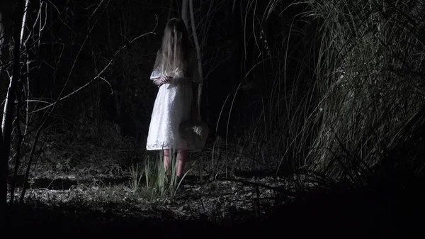 Ένα μικρό κορίτσι φάντασμα με μακριά μαύρα μαλλιά, λευκό, περιφέρεται μέσα στο δάσος με ένα μαχαίρι και ένα μαλακό παιχνίδι. — Φωτογραφία Αρχείου