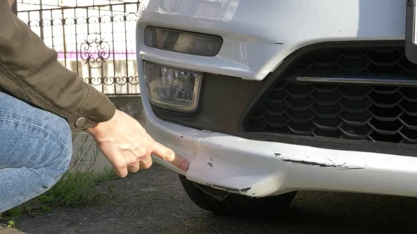 A olhar para um veículo danificado. Mulher inspeciona danos no carro após um acidente — Fotografia de Stock