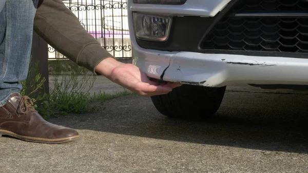 A olhar para um veículo danificado. homem inspeciona danos no carro após um acidente — Fotografia de Stock