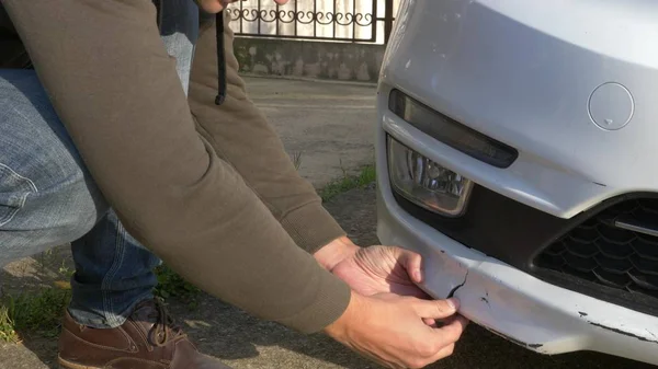 A olhar para um veículo danificado. homem inspeciona danos no carro após um acidente — Fotografia de Stock