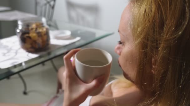 Голодная грустная женщина сидит в гостиной за столом ночью, ест печень и пользуется смартфоном — стоковое видео