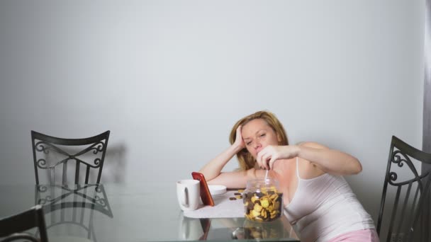 Mujer triste hambrienta se sienta en una sala de estar en una mesa por la noche, se come un hígado y utiliza su teléfono inteligente — Vídeos de Stock