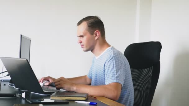 Un homme assis à un bureau à la maison, travaillant à la maison ordinateur et ordinateur portable . — Video