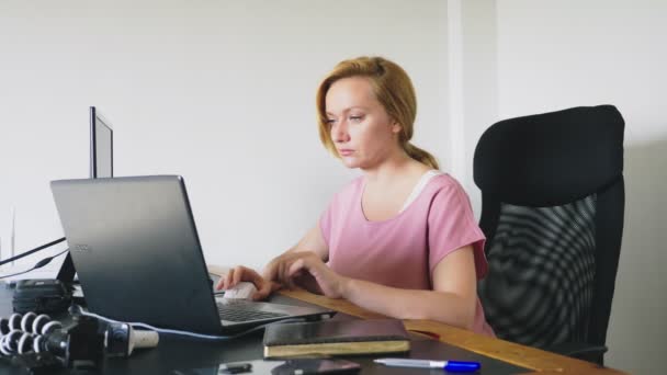 Bela jovem mulher trabalhando em um laptop e computador enquanto sentado em uma mesa . — Vídeo de Stock