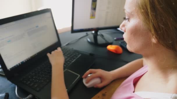 Bela jovem mulher trabalhando em um laptop e computador enquanto sentado em uma mesa . — Vídeo de Stock